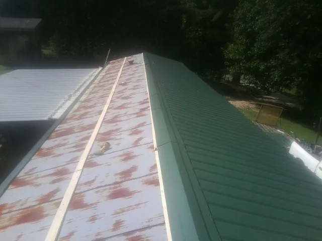 Old rusted panels beside newly installed green metal roofing — Wind Damage Roof Repair by Roofing Brothers in Saluda
